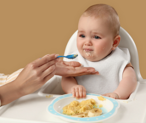 Baby beim entspannten Beikoststart mit Löffel im Hochstuhl